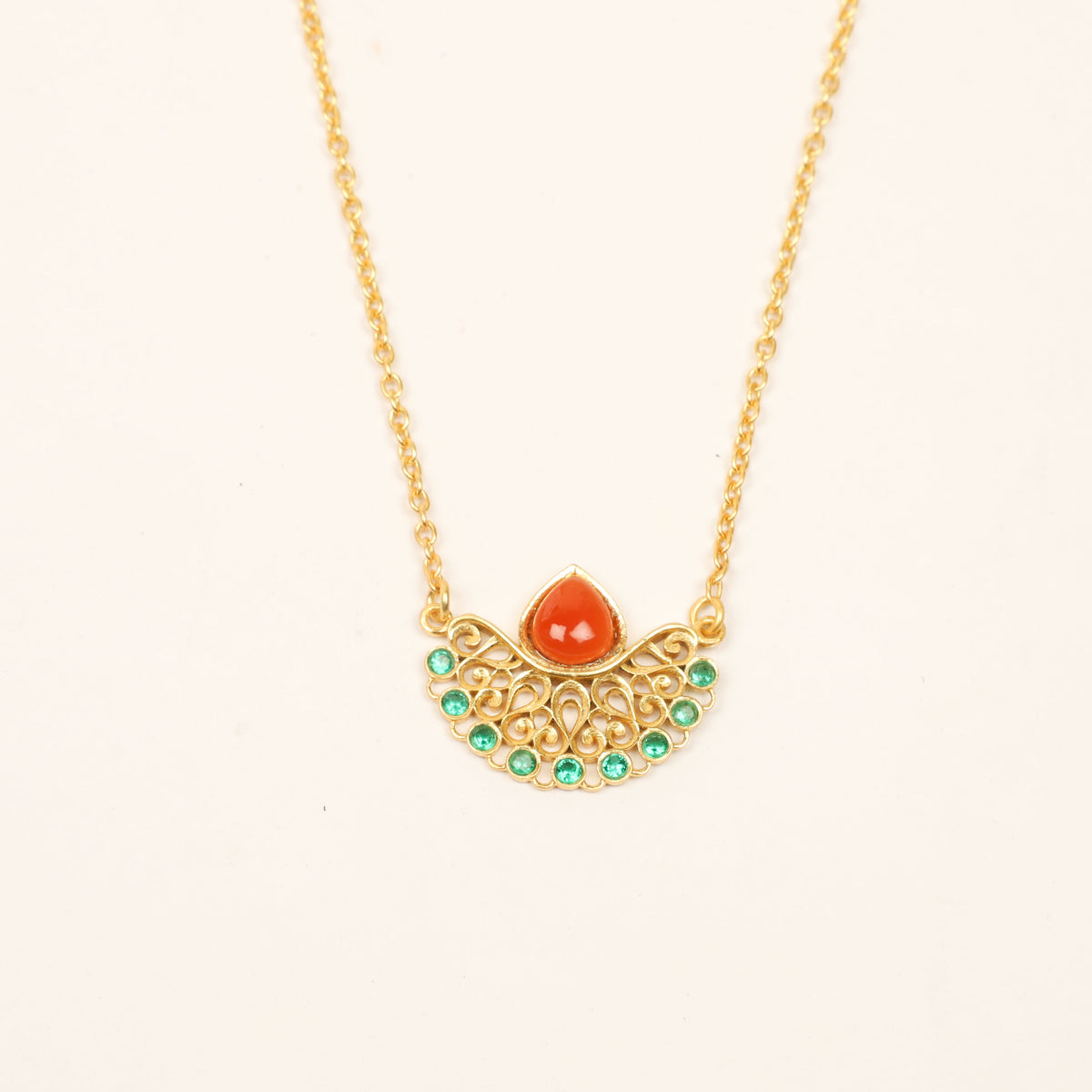 Gold necklace with a decorative pendant featuring a red teardrop-shaped stone and small green stones, shown on a plain light background.