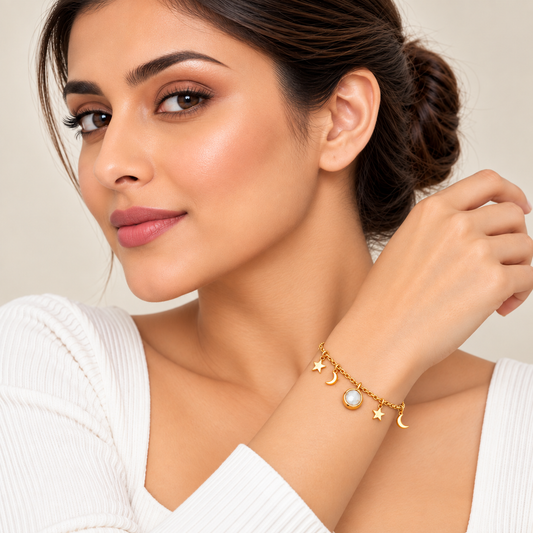 A woman wearing a delicate gold charm bracelet with crescent moon, star, and pearl charms, posing against a soft beige background.

