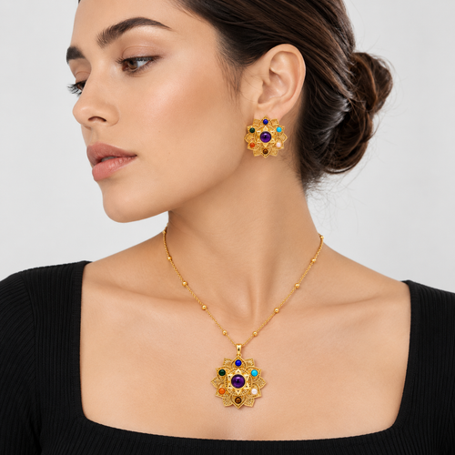 A woman wearing a gold necklace with a matching flower-shaped pendant and matching stud earrings, featuring multicolored gemstone accents, set against a light gray background.


