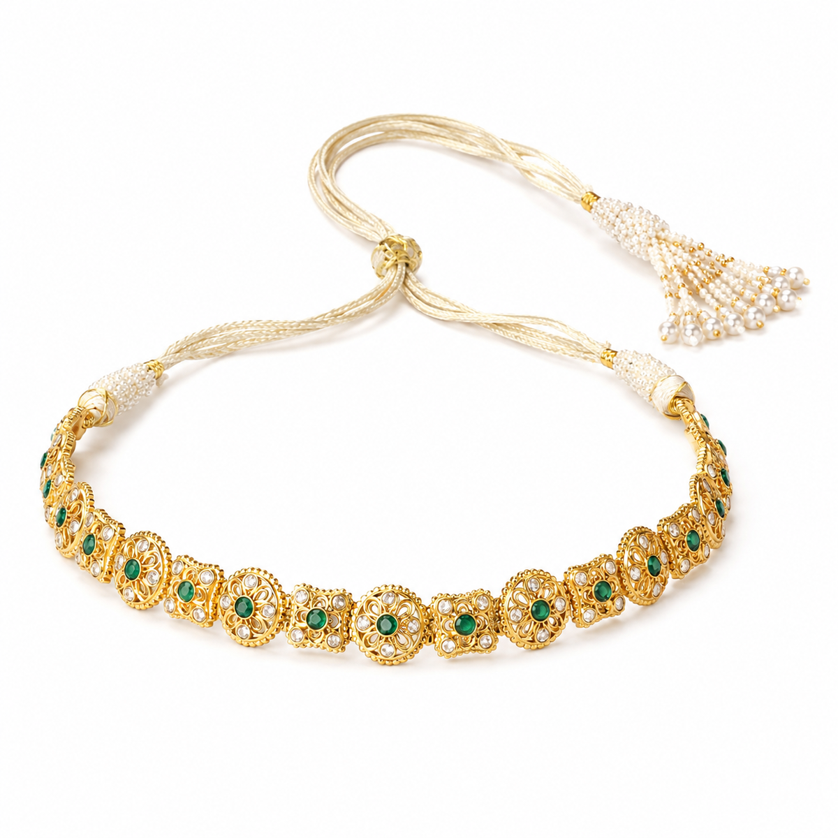 Gold-plated traditional Indian jewelry piece featuring intricate filigree patterns, green stone accents, and a tassel with white stones on a white background.


