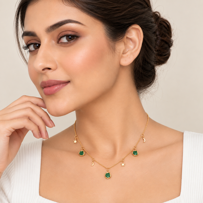A woman wearing a delicate gold necklace with green gemstone charms shaped like stars, crescent moons, and a central pendant, styled with matching stud earrings against a soft beige background.

