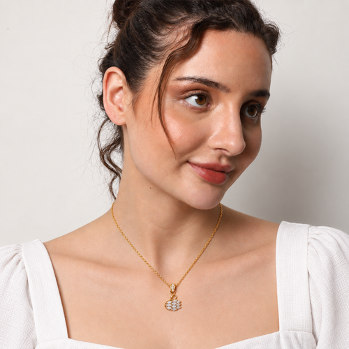 A woman wearing a delicate gold chain necklace with a small, diamond-like cluster pendant, photographed against a clean, light off-white background.

